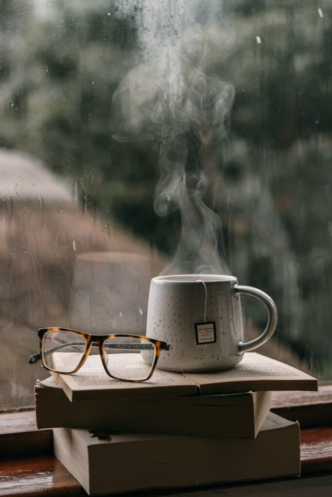 Quiet Time, cup of tea, books, reading glasses in front of a rainy day window